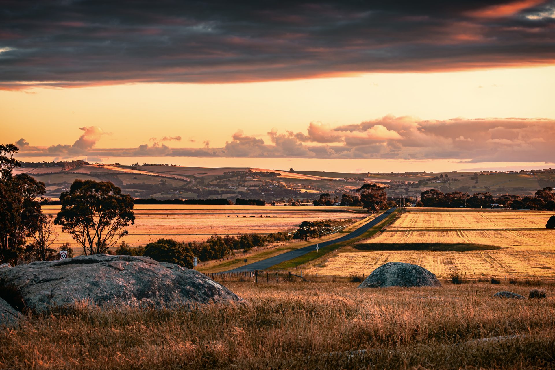 A country road running through harvested paddocks and rolling farmland at sunset