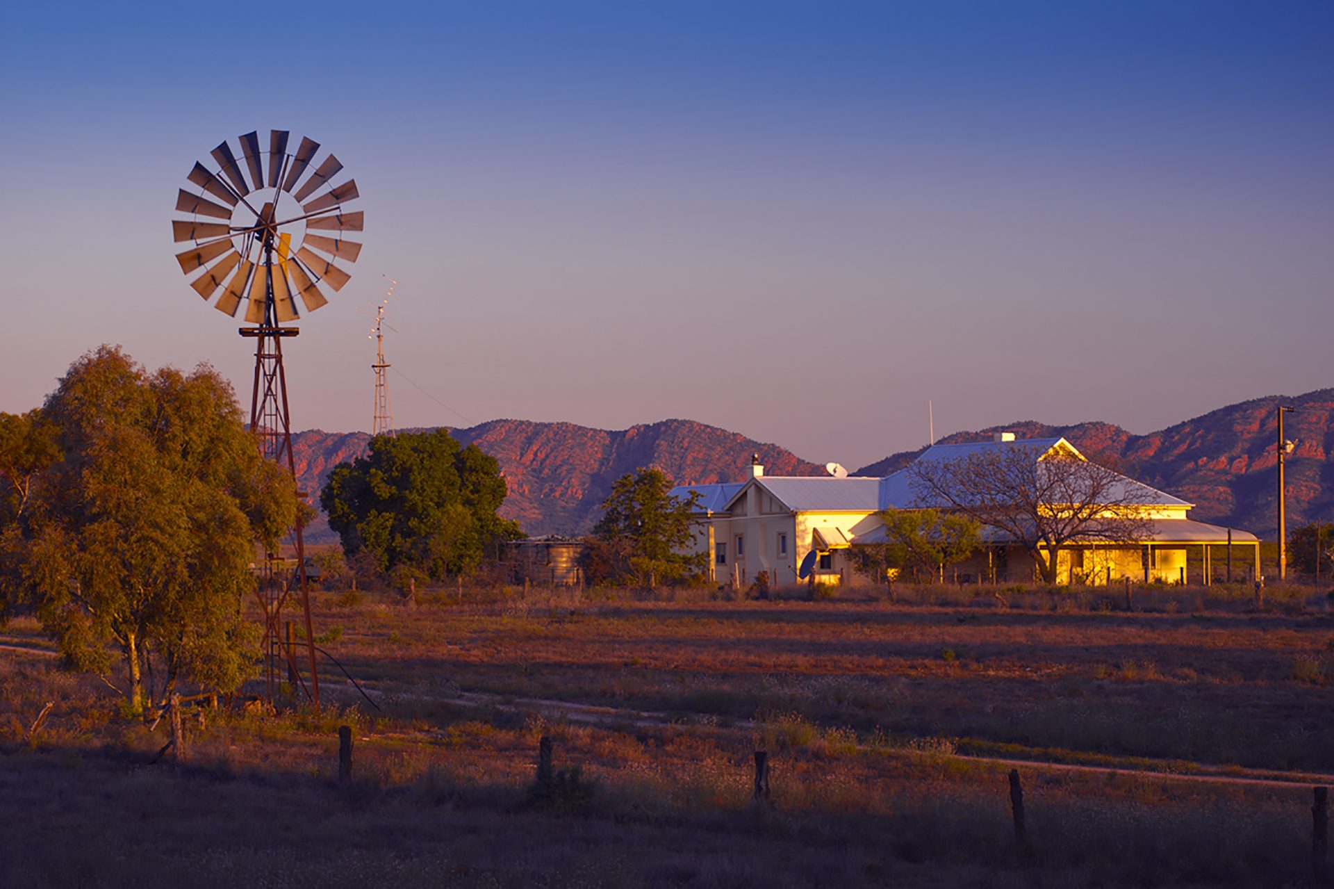 A farm homestead and windmill below red ranges in the last light of the day