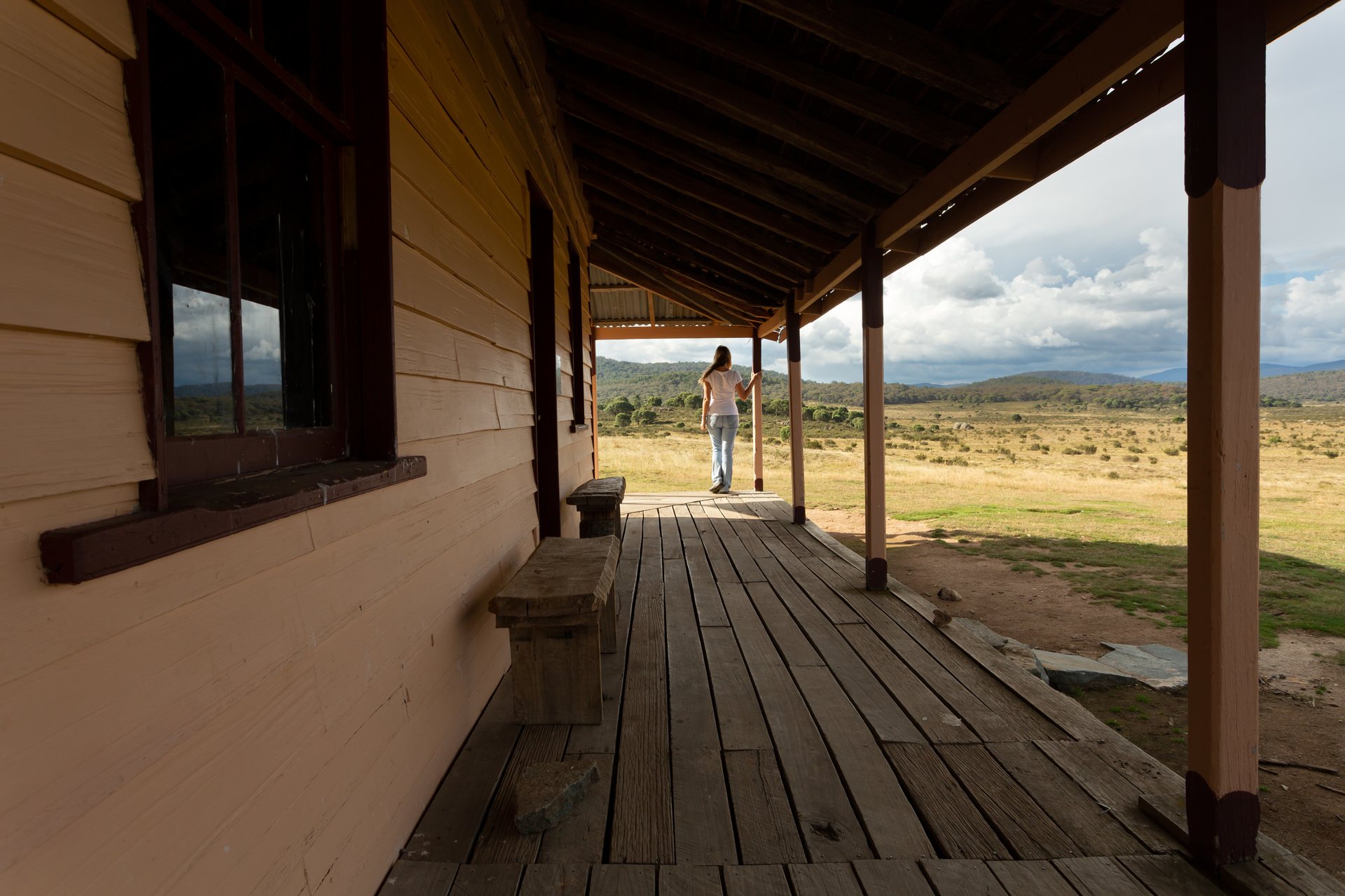 A figure on the veranda of a weatherboard high-country homestead, looking out across the plains
